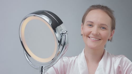 Woman Smiles Looking at Herself in Lighted Mirror