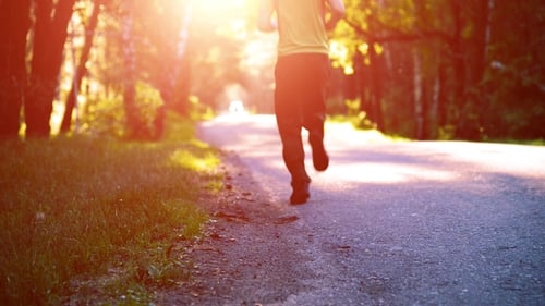 Sport Man Running at Asphalt Road. Rural City Park. Green Tree Forest and Sun Rays on Horizon.