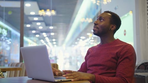 Portrait of Happy African Businessman Sitting in a Cafe and Working on Laptop