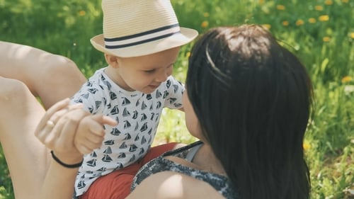 Happy Young Mother Playing on Blanket with Her Cute Son Under Tree at Park