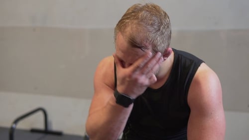 Tired Fitness Man Resting After Workout and Wiping Sweat From His Face at Gym