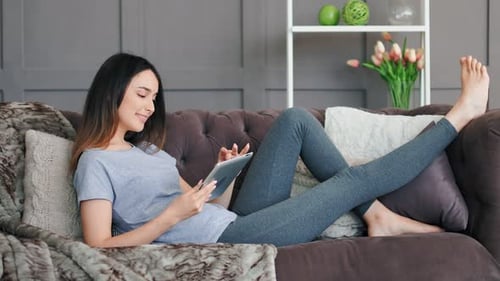 Woman Relaxes on Couch Using Tablet