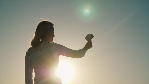 A Woman Is Playing with a Paper Airplane. It Stands in the Rays of the Setting Sun. Dreams About