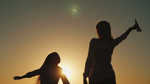 Woman and Child Play with Paper Airplane at Sunset
