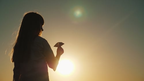 Child Silhouette with Paper Airplane at Sunset
