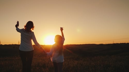 Mom and Daughter Are Playing Paper Airplanes at Sunset. In a Picturesque Place. Happy Time with the