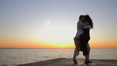 Silhouettes of Young Hispanic Couple Against Sunset Sea Background. Man and Woman Dancing Latin