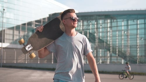 Young Adult Carries Skateboard in Urban Setting