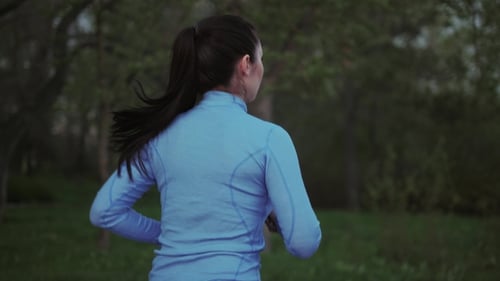 A Young Girl in Blue Sports Clothes Is Running Along the Evening Park Back View