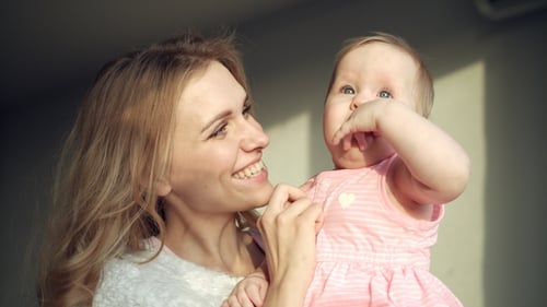 Happy Mother Holding Baby Girl on Hands. Cheerful Mom Embrace Toddler Girl