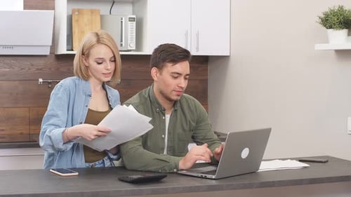 Couple Reviewing Documents and Laptop in Kitchen