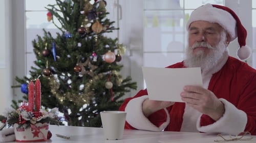 Santa Claus Reading Letter by Decorated Christmas Tree