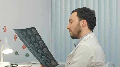 Concentrated Male Doctor Looking at X-ray Picture in the Medical Office