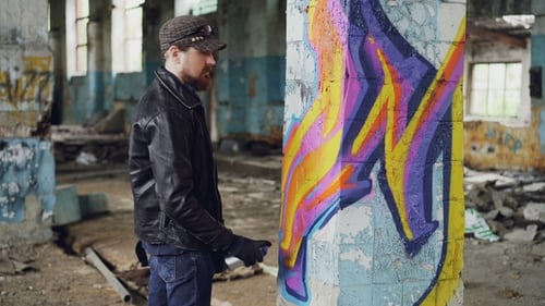 Professioneller Graffiti-Maler schafft abstrakte Bilder auf einer großen Säule in einem verlassenen Gebäude