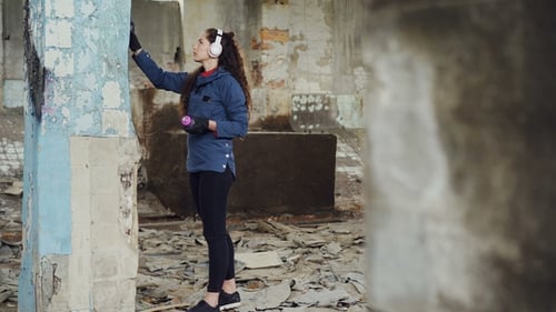 Tiro inclinado do pintor urbano moderno desenhando graffiti no pilar alto em armazém abandonado com