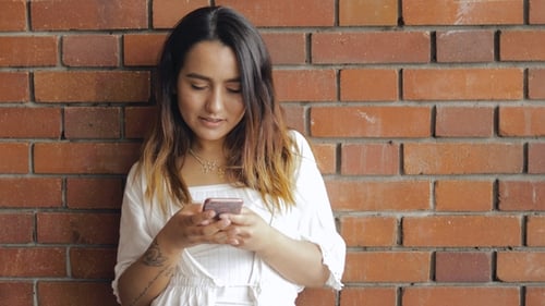 Woman Using Phone By a Red Brick Wall