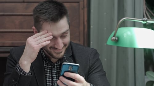 Smiling Man Uses Phone Indoors at Table