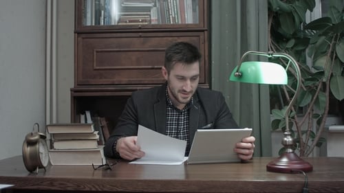 Young Professor Having a Video Call Via Tablet To Discuss Paper Written By His Student
