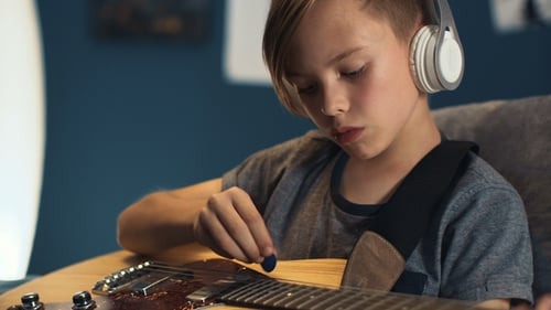Child Plays Electric Guitar with Headphones Indoors