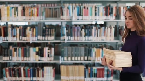 Smiling Female Student Hold Books Walking Before the Shelves in the Library