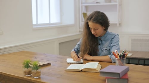 Girl Studying at Table Writing in Notebook