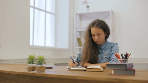 Girl Writing in Notebook at Wooden Table