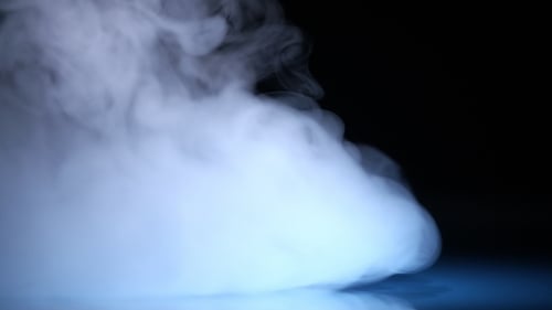 Weiße kalte Nebelwolke im blauen Lichtfleck auf schwarzem Hintergrund in
