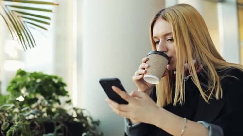 Joven mujer de negocios escribe algo en su teléfono inteligente sentada en un café