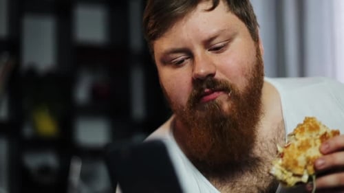 Bearded Man Eating Hamburger Looking at Phone, Close Up