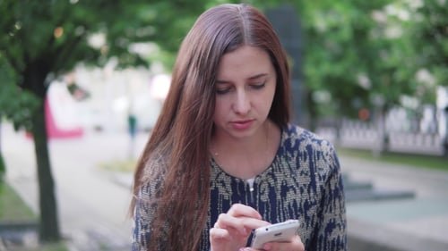 A Young Woman Uses a Mobile Phone in the City