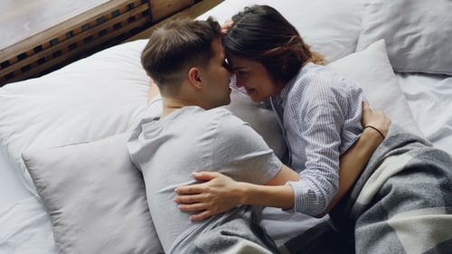 Attractive Mixed-race Couple Is Lying in Bed and Talking, Caressing Each Other and Laughing