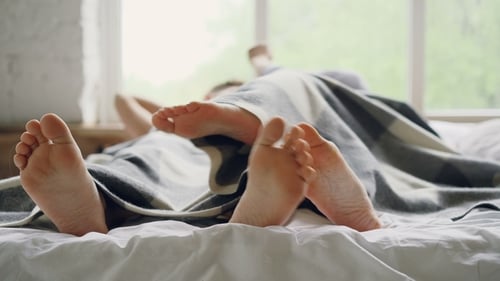 Ehemann und Ehefrau liegen im Bett unter einer Decke und reden und umarmen sich dann