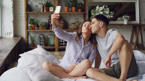 Fröhlich liebendes Paar macht Selfie mit Smartphone und schaut in die Kamera, posiert und macht lustig