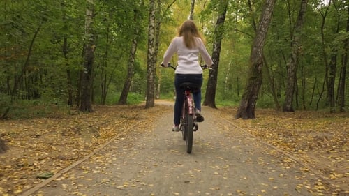 Young Woman Is Riding Bicycle in the Park Autumn and Falling Yellow Leaves