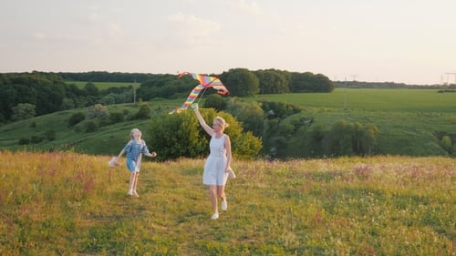 Mother and Daughter Running with Kite in Green Meadow