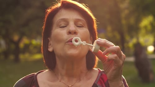 Adult Woman Blowing Bubbles in a Sunny Park