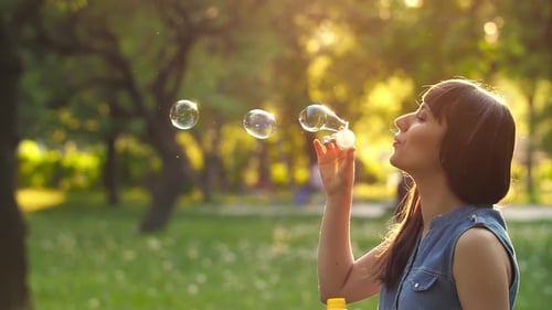 Woman Blowing Bubbles in Park at Sunset