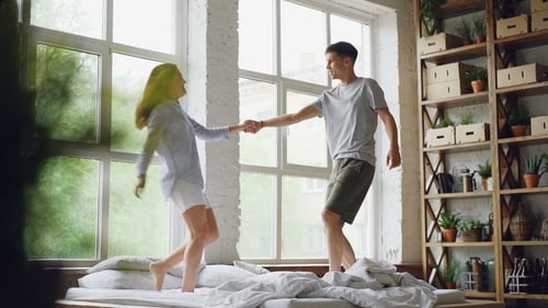 Cheerful Couple Dancing on Bed in Bright Room