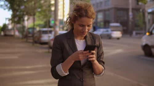Woman Uses Phone on City Street Sidewalk
