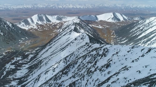 Snowy Mountain Ridge at Sunny Day. Aerial View. Drone Is Flying Forward. Camera Is Tilting Up