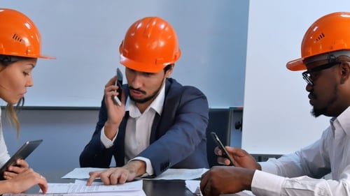 Tres colegas en cascos discuten el plan de restricción mediante el uso de tabletas digitales y teléfonos inteligentes
