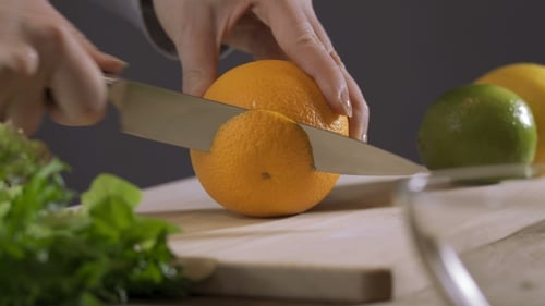 Orange von Hand auf Holzbrett schneiden.