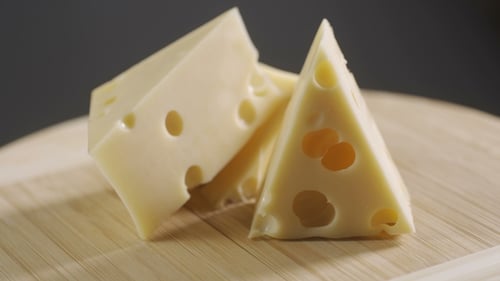 Käse, in Stücke geschnitten auf einem Holzteller. Dreht sich vor einem grauen Hintergrund