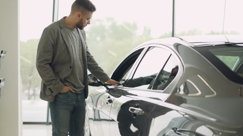 Stylish Guy Is Choosing New Automobile Walking Around Luxury Car and Touching It in Car Dealership