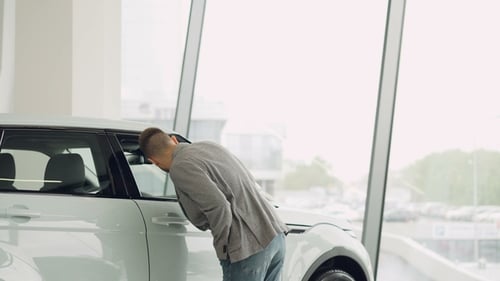 Confident Young Man Is Looking at Car in Automobile Showroom