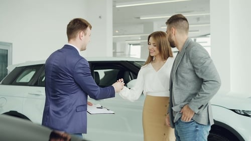 Cheerful Car Dealership Salesman Is Shaking Hands with Young Buyer Handsome Man Then Giving Key