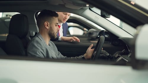 Confident Man Car Buyer Is Sitting in Driver's Seat in New Automobile Inside Modern Showroom and