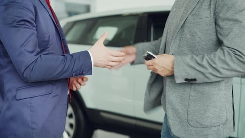 Male Worker of Car Showroom Is Giving Car Keys To Buyer Young Man and Shking Hands with Him Standing