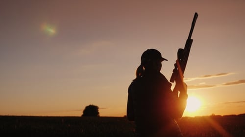 Eine Frau mit einer Pistole geht über das Feld. Der Beginn der Jagdsaison. Ansicht von hinten