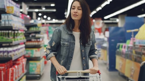 Attractive Woman Is Driving Shopping Trolley Through Food Department in Supermarket and Looking